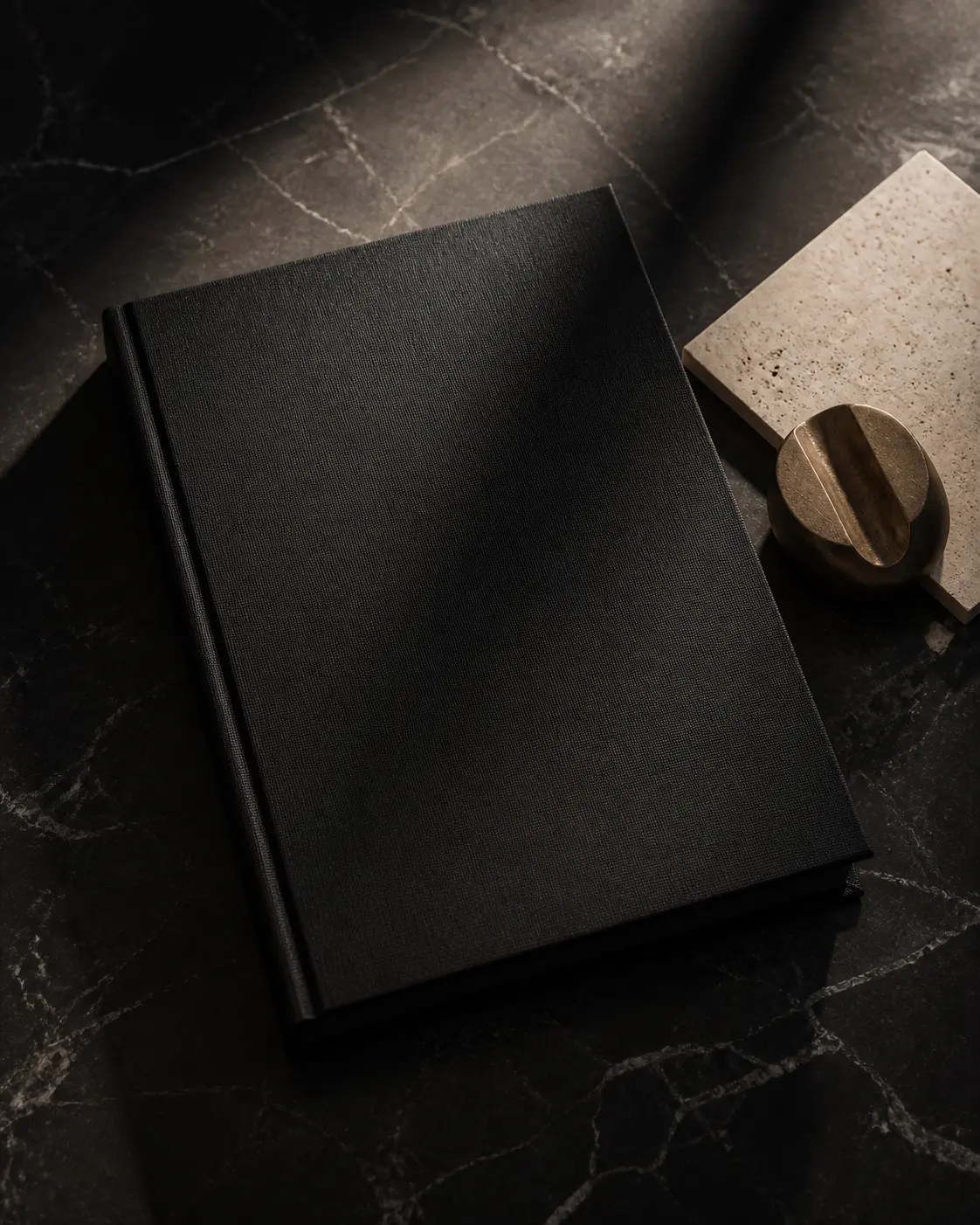 A black linen-bound portfolio lying closed on a dark marble surface, lit softly from one side.